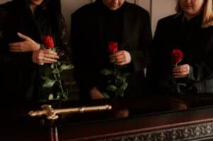 Begravelsetraditioner i Danmark - billede af sørgende der står ved kisten med en rose hver i hånden.